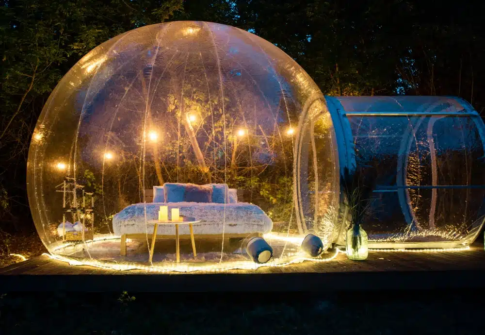 Transparent bubble tent with bed and string lights in nature.
