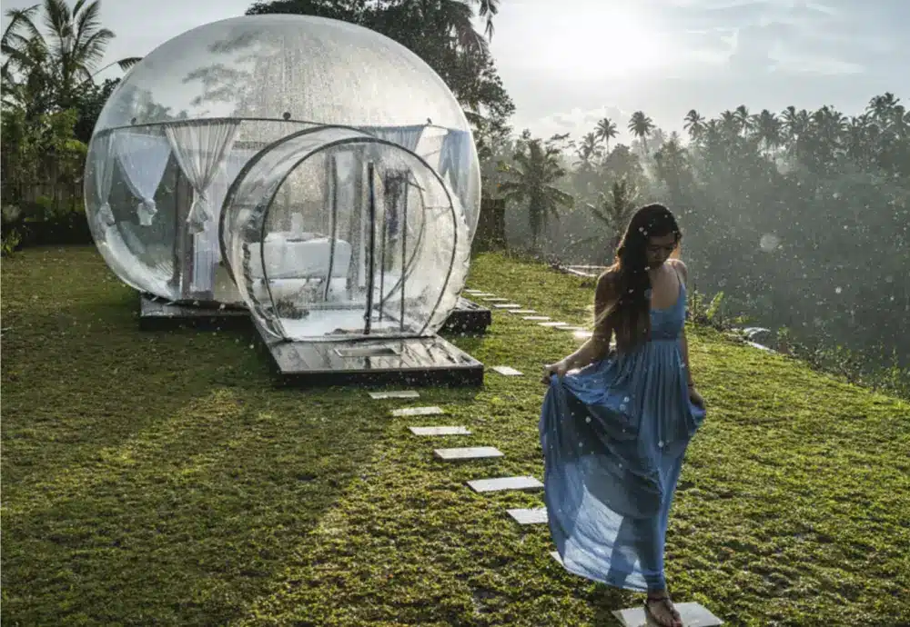 Woman in blue dress walking toward a clear bubble dome on a grassy hill.