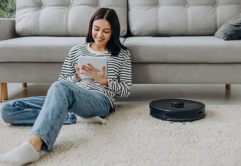 Woman relaxing with tablet while robot vacuum cleans carpet.