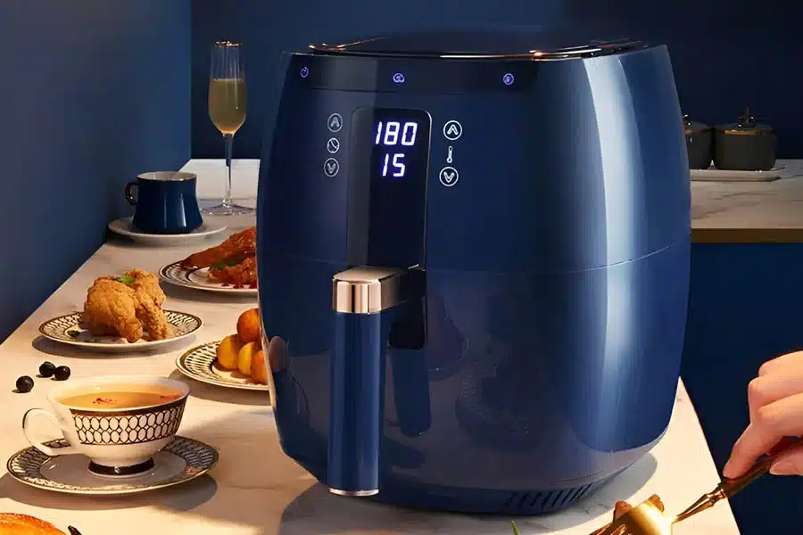 Sleek navy blue air fryer on a table surrounded by plates of food and a champagne glass.