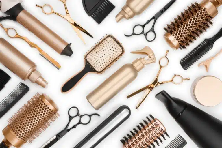 Flat lay of professional hair styling tools including brushes, scissors, and a hairdryer on a white background.