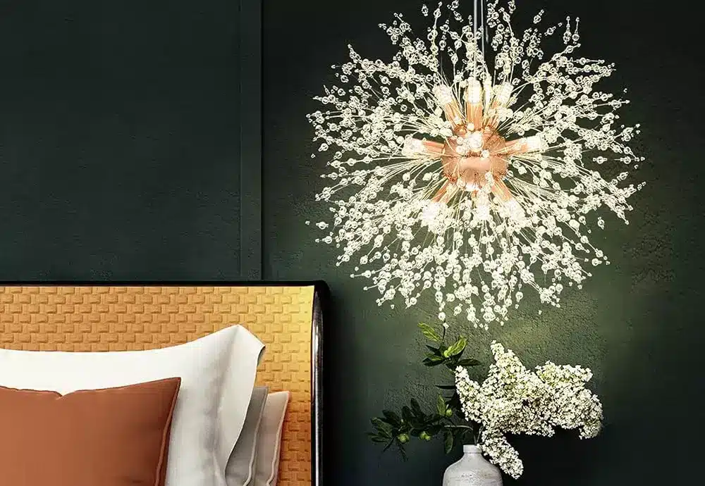 Modern starburst chandelier casting warm light above a cozy bed and flower arrangement.