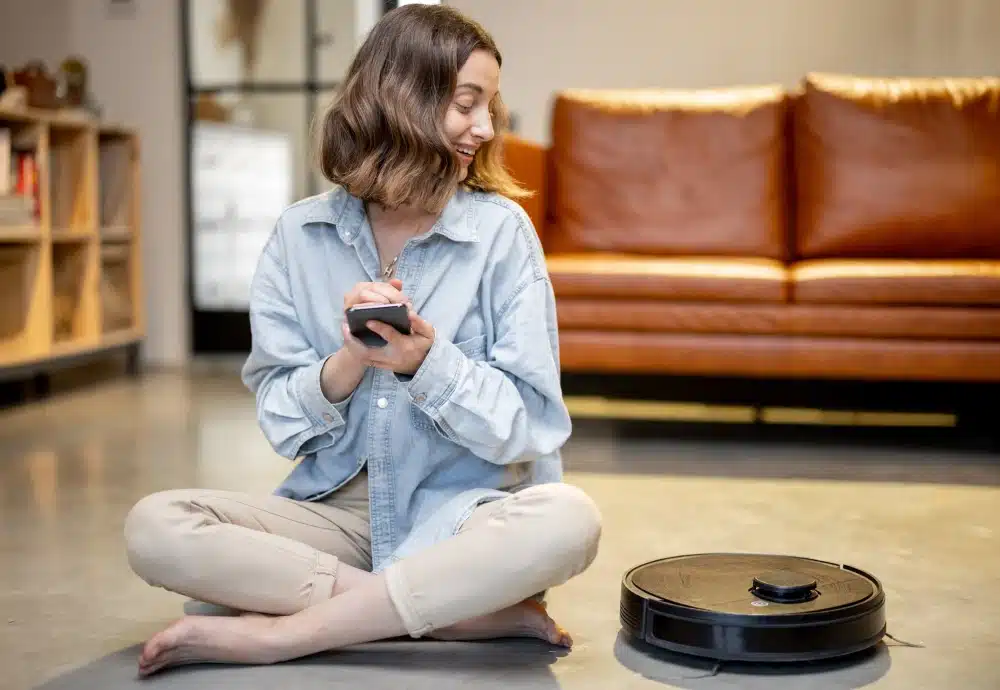 Woman controls robot vacuum cleaner with smartphone at home.