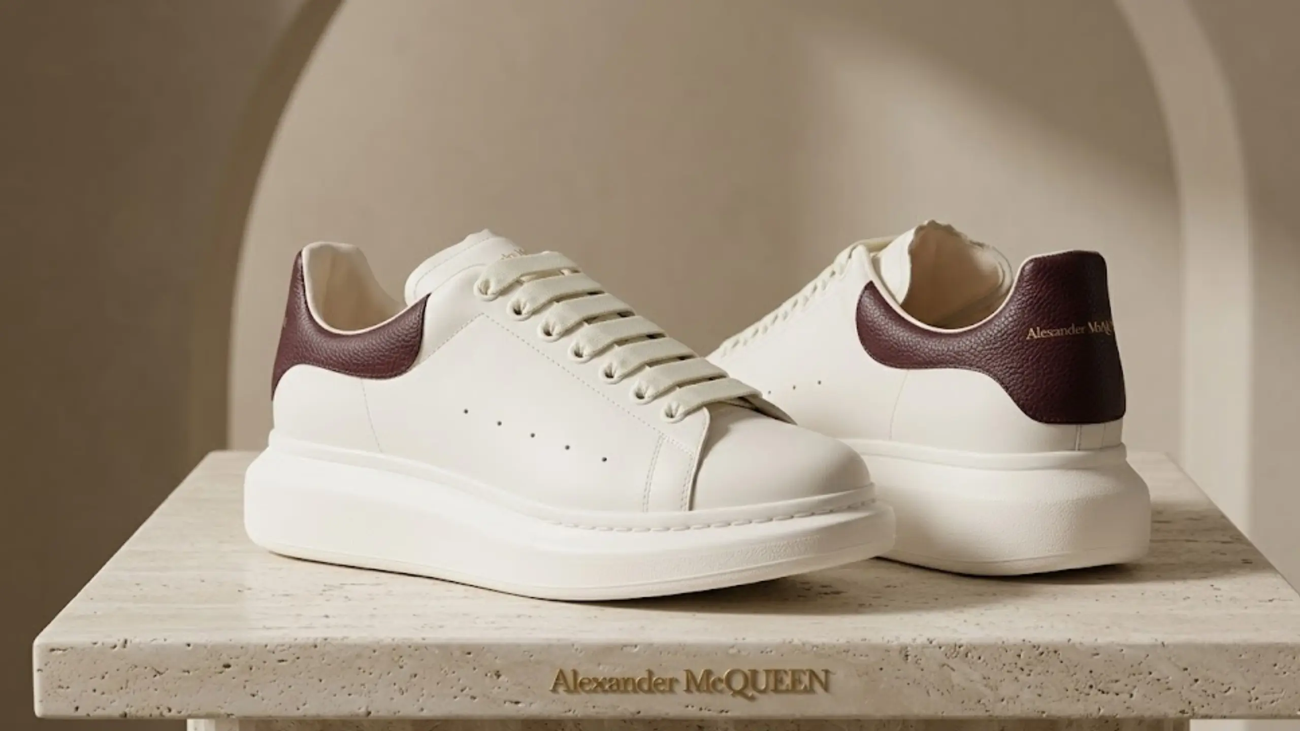 McQueen platform sneakers in white leather with burgundy heel tab displayed on a minimalist luxury stone platform