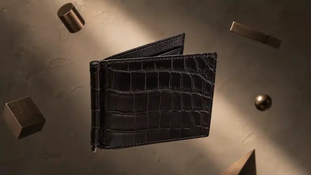 Classic designer wallets :Bottega Veneta Crocodile Wallet in black textured croc leather with signature intrecciato stitching and metal clasp, floating amid geometric bronze shapes.