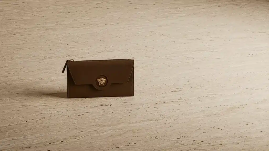 Versace brown leather wallet with gold Medusa emblem on stone, representing eco-friendly luxury brands.